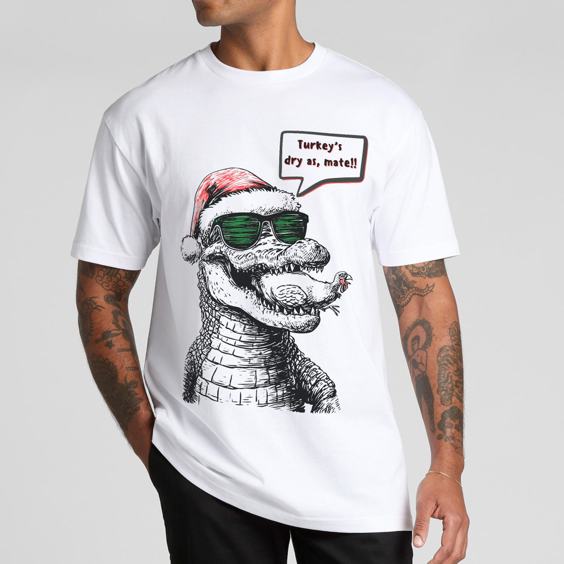 Person wearing a white t-shirt with a graphic of a crocodile eating a turkey wearing sunglasses and a Santa hat,