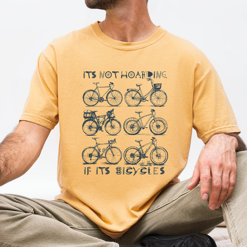A man wearing a mustard yellow graphic t-shirt with a black bicycle design and the text 'ITS NOT HOARING IF ITS BICYCLES'.