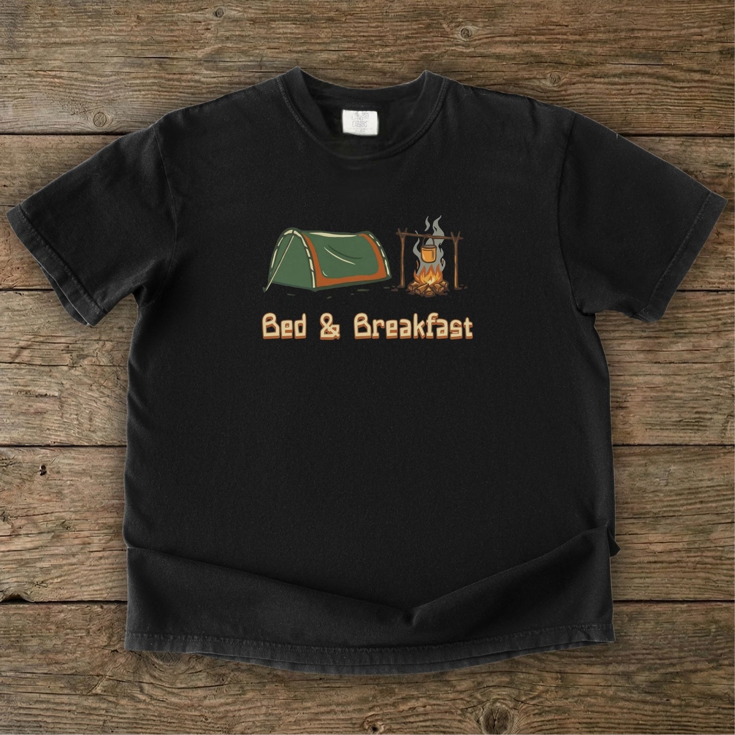 Black t-shirt with camping graphic and 'Bed & Breakfast' text on a wooden surface