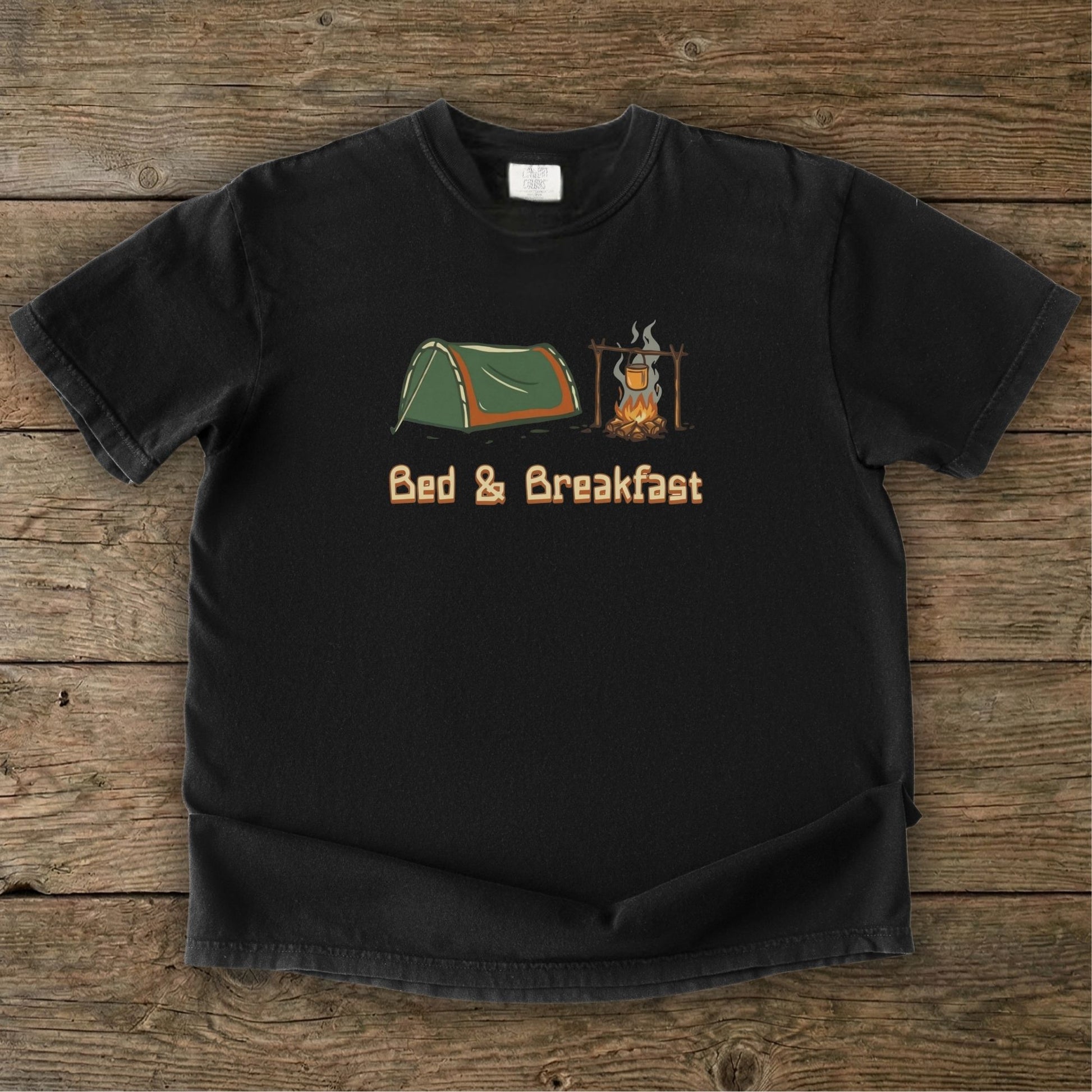 Black t-shirt with camping graphic and 'Bed & Breakfast' text on a wooden surface