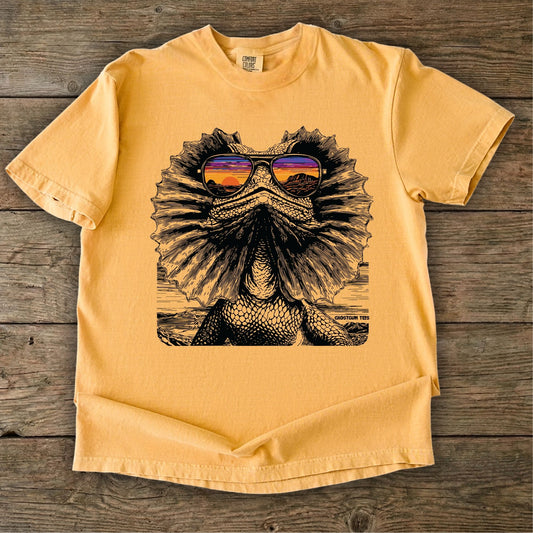 Yellow t-shirt with a graphic of a Frilled neck lizard wearing sunglasses on a wooden surface