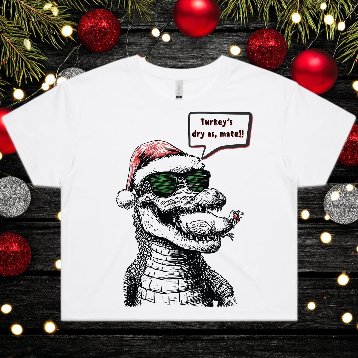 White t-shirt with a graphic of a crocodile wearing a Santa hat and sunglasses, surrounded by Christmas decorations.