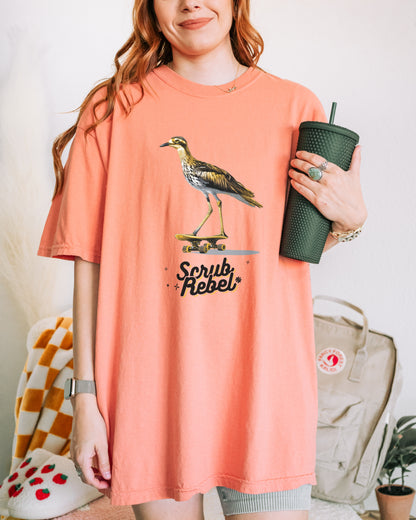 Person wearing a peach t-shirt with a bush stone curlew bird graphic and 'Scrub Rebel' text, holding a green tumbler.