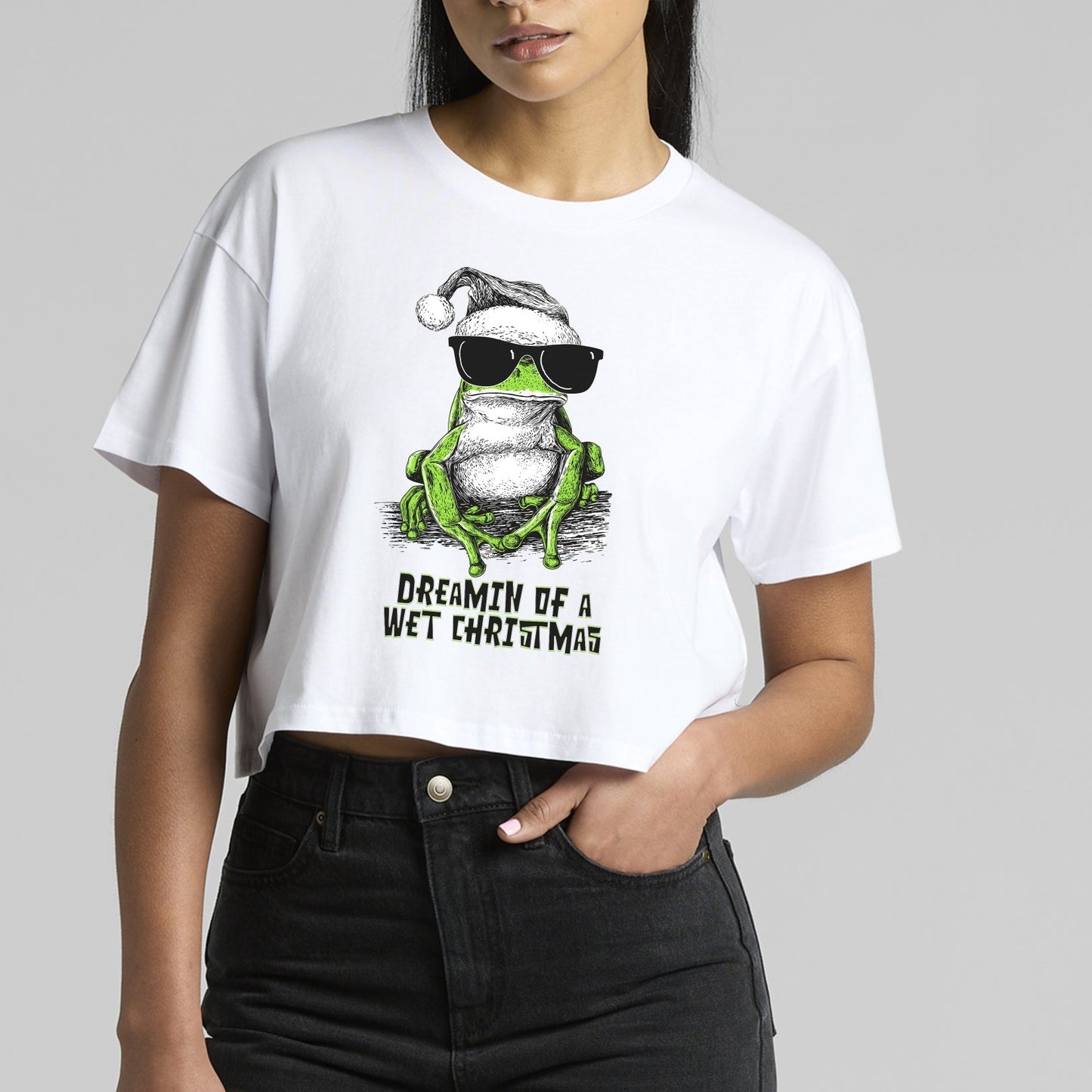 Green tree frog Christmas T-shirt — illustrated frog wearing sunnies and a Santa hat with the text “Dreamin’ of a Wet Christmas” printed on a white tee.