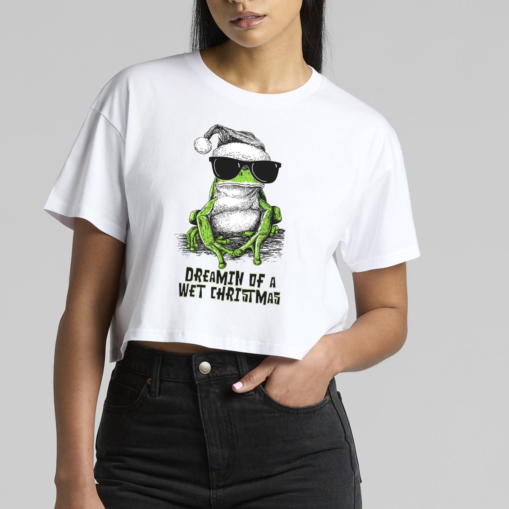 Green tree frog Christmas T-shirt — illustrated frog wearing sunnies and a Santa hat with the text “Dreamin’ of a Wet Christmas” printed on a white tee.