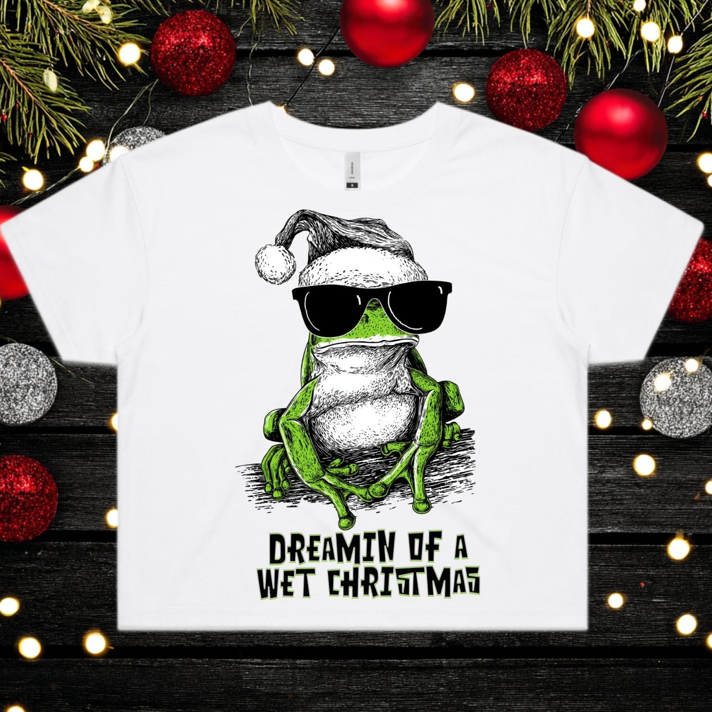 White t-shirt with a frog wearing sunglasses and a Santa hat, surrounded by Christmas decorations.