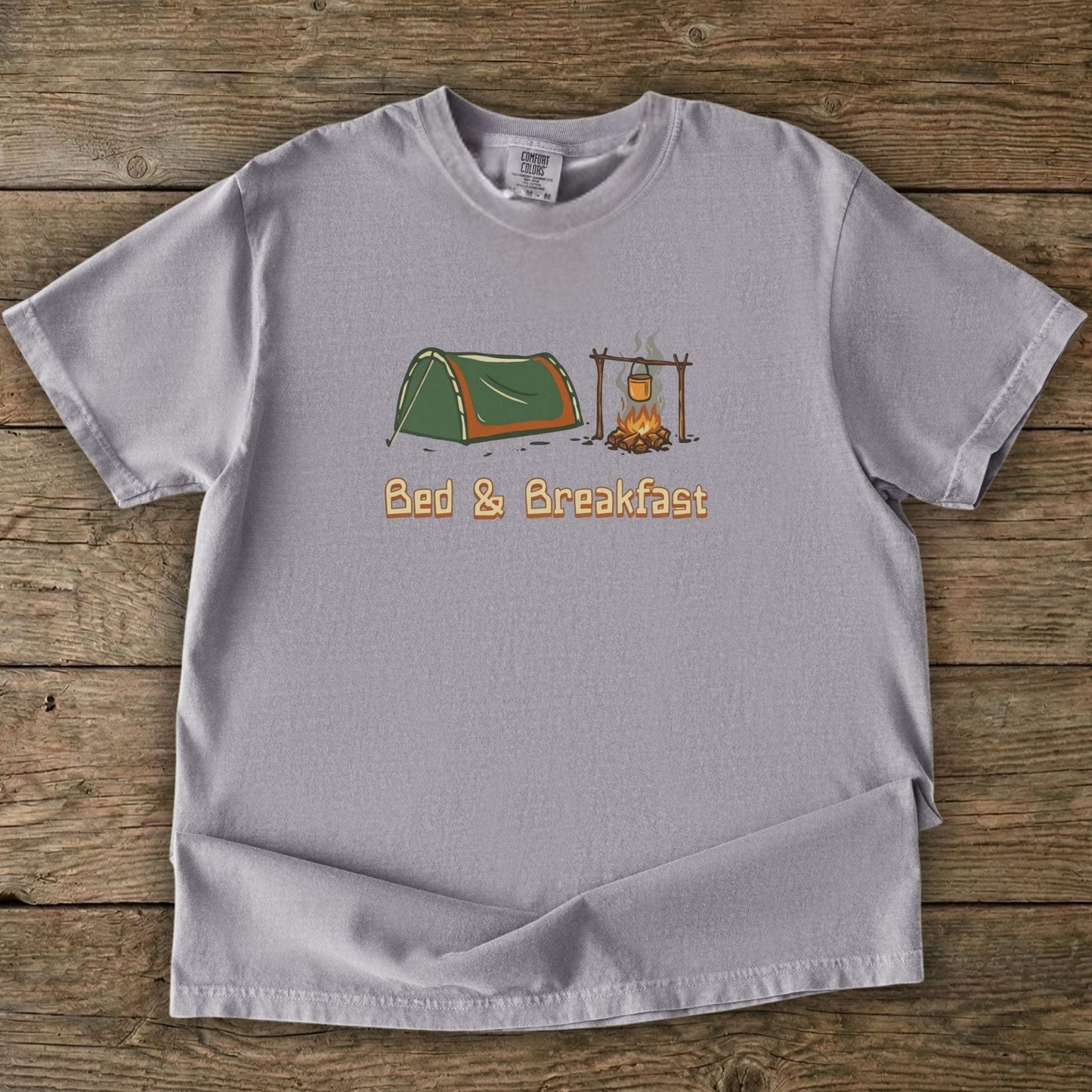 Gray t-shirt with camping graphic and 'Bed & Breakfast' text on a wooden surface