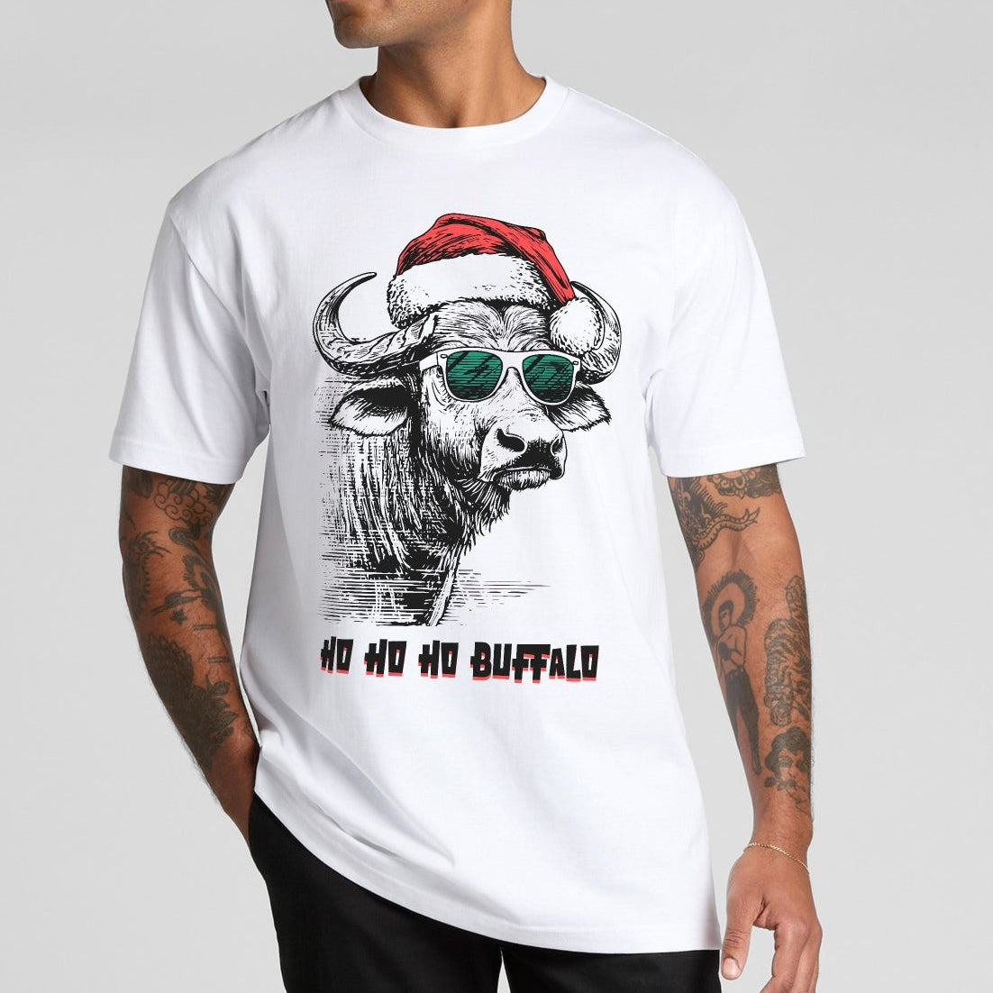 Person wearing a white t-shirt with a graphic of a buffalo wearing a Santa hat and sunglasses, text 'Ho Ho Ho Buffalo' on a gray background.