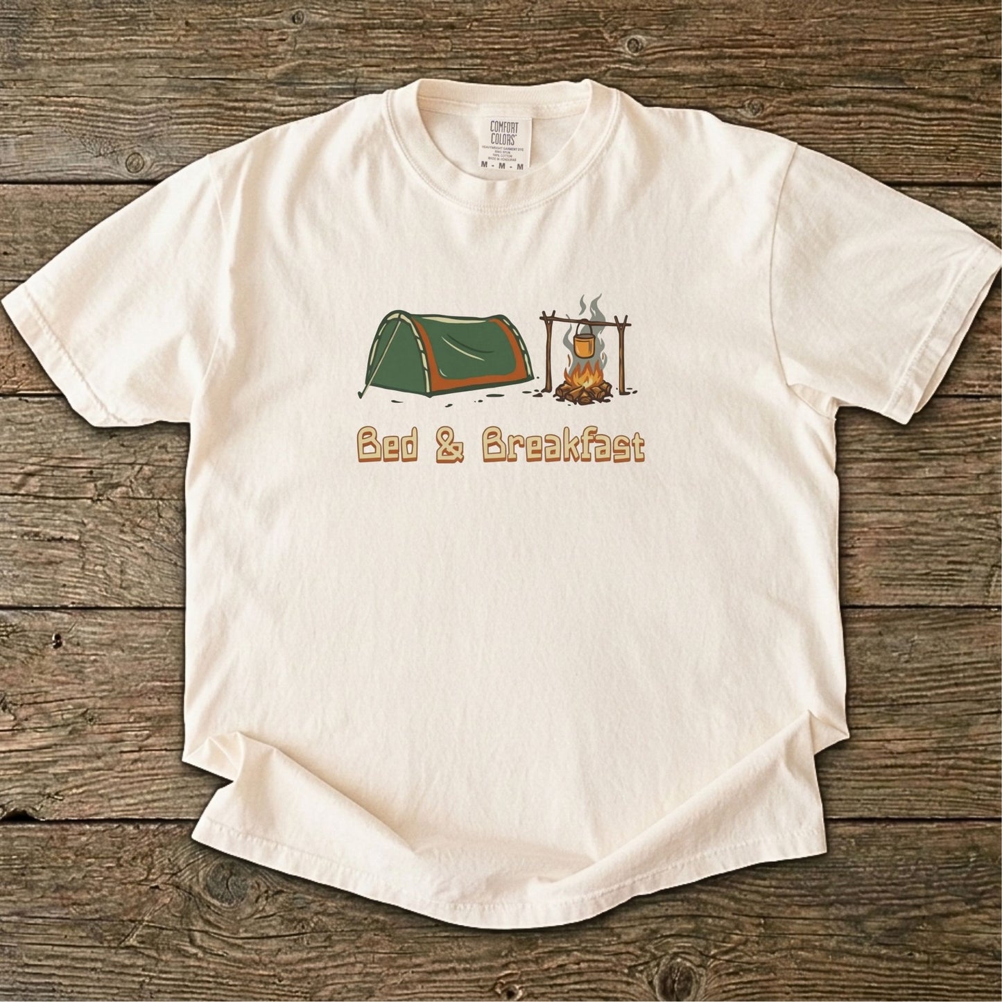 Ivory t-shirt with camping graphic and 'Bed & Breakfast' text on a wooden surface
