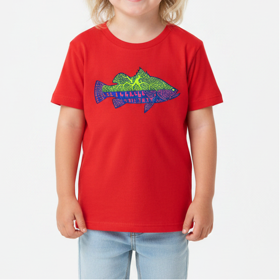 A young child with blonde hair stands against a white studio background wearing a bright red short-sleeve t-shirt with a colorful fish graphic on the chest, light blue denim shorts, and white sneakers.