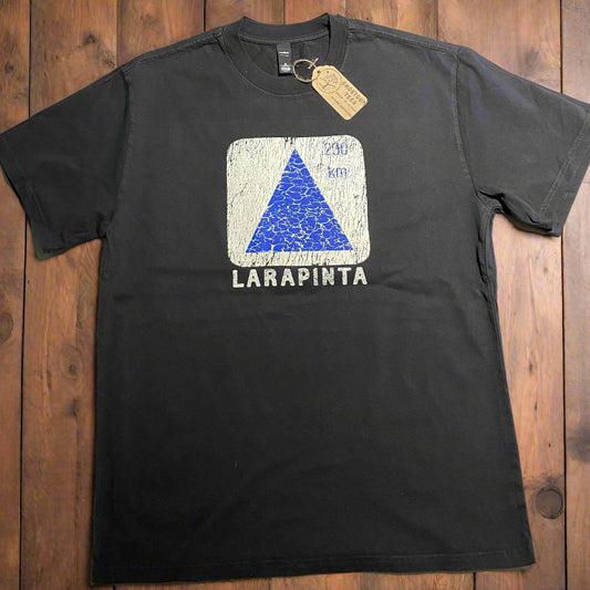 Black t-shirt with a white square graphic design featuring a blue trail marker triangle and 'LARAPINTA' text on a wooden background.