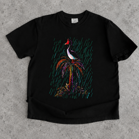 A black short-sleeve crewneck t-shirt featuring a colorful graphic print of a rmagpie goose bird perched on a palm tree under diagonal rain streaks.