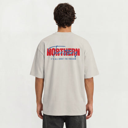 A man viewed from behind wearing a light beige t-shirt with a large red and blue graphic on the back that reads 'NORTHERN Territory IT'S ALL ABOUT THE FREEDOM'.