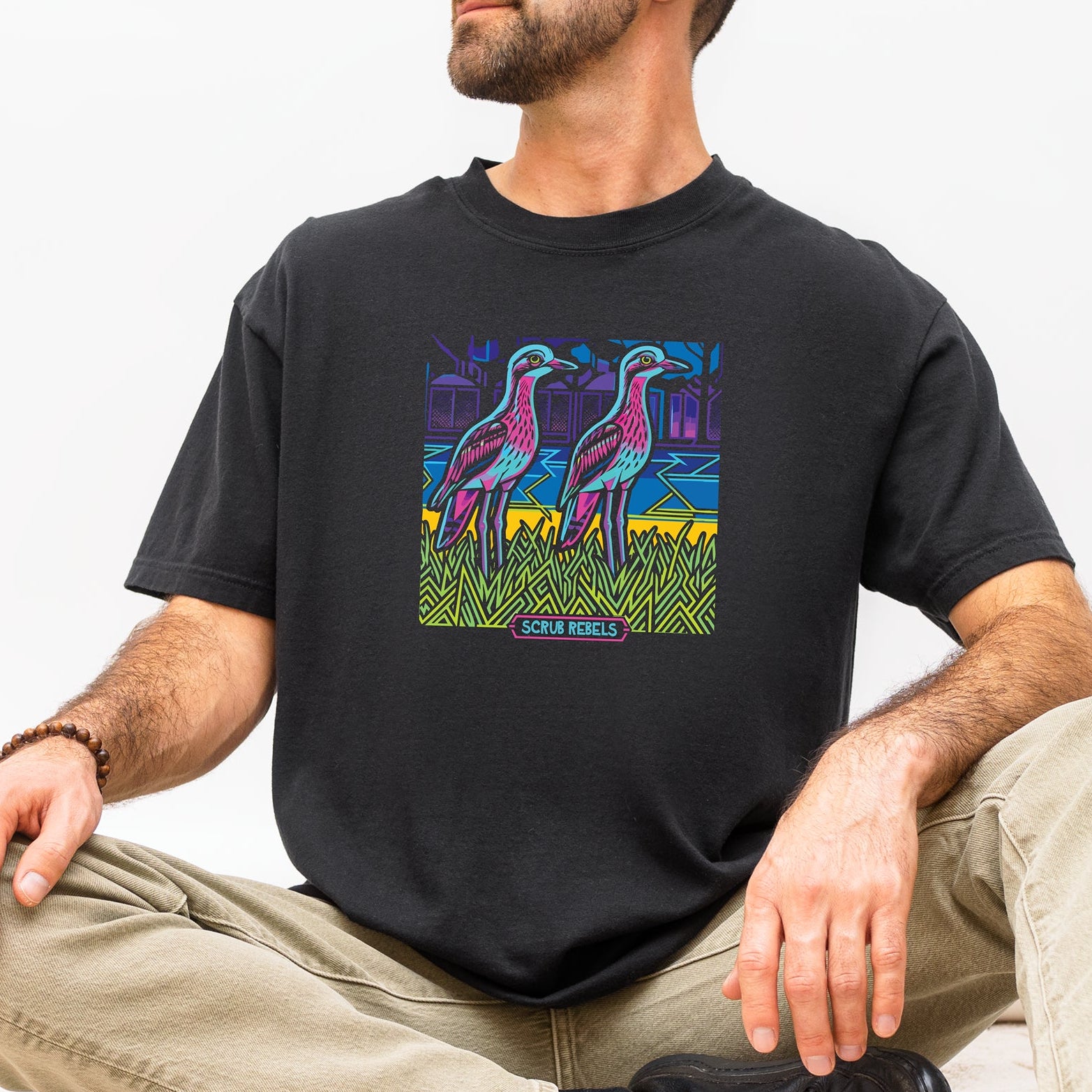 Person wearing a black t-shirt with colorful curlew graphic design sitting on a white background