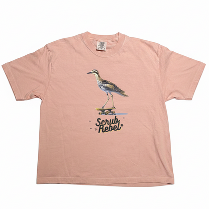 A light pink short-sleeve t-shirt with a graphic of a heron bird on a skateboard and the text 'Scrub Rebel' printed on the front, displayed flat against a white background.