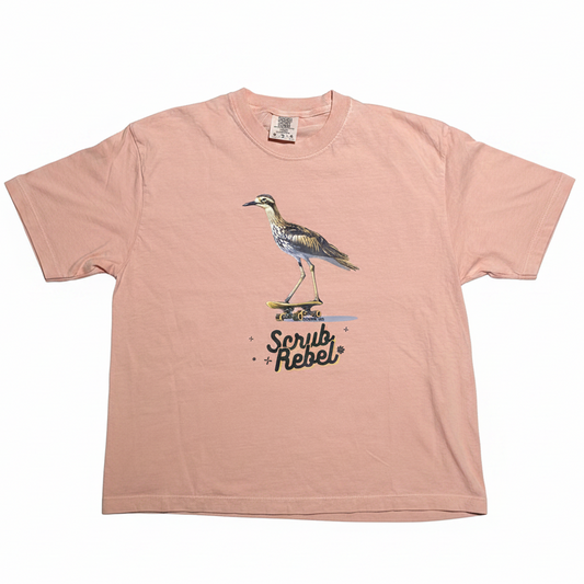 A light pink short-sleeve t-shirt with a graphic of a heron bird on a skateboard and the text 'Scrub Rebel' printed on the front, displayed flat against a white background.