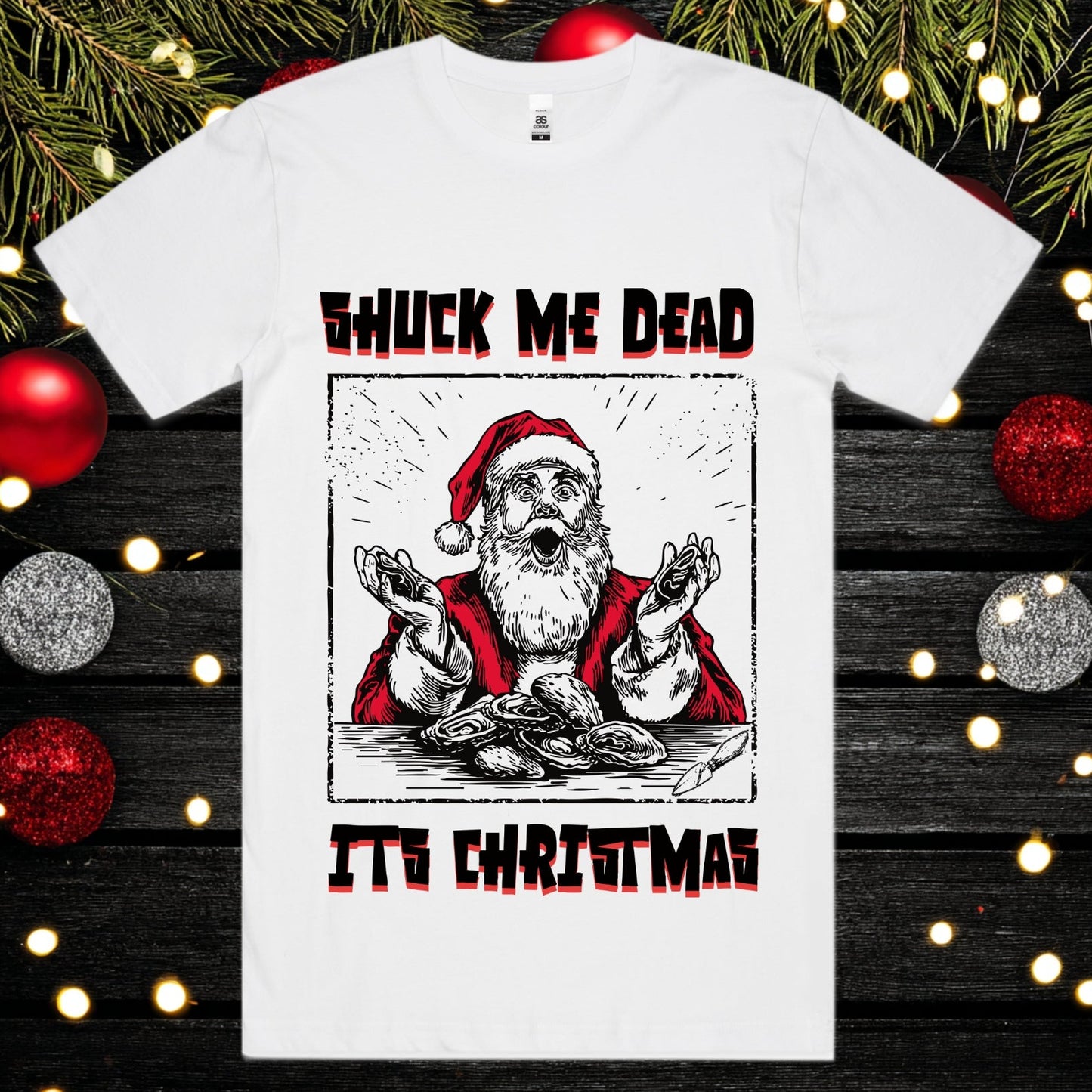 White t-shirt with a graphic of Santa Claus and text 'Shuck Me Dead It's Christmas' on a festive background.