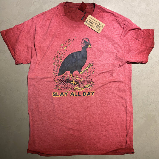 A heathered red short-sleeve graphic t-shirt laid flat on a gray surface. The shirt features a graphic of a bush chook with yellow accents and the text 'SLAY ALL DAY' printed on the front, with a paper brand tag still attached to the collar.