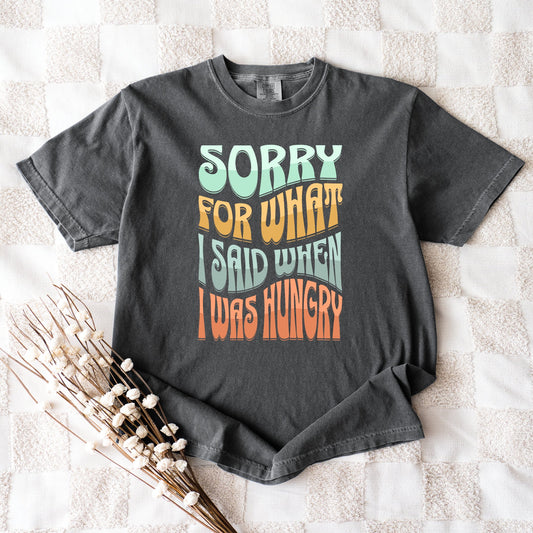 Gray t-shirt with colorful text on a textured surface with dried plants.