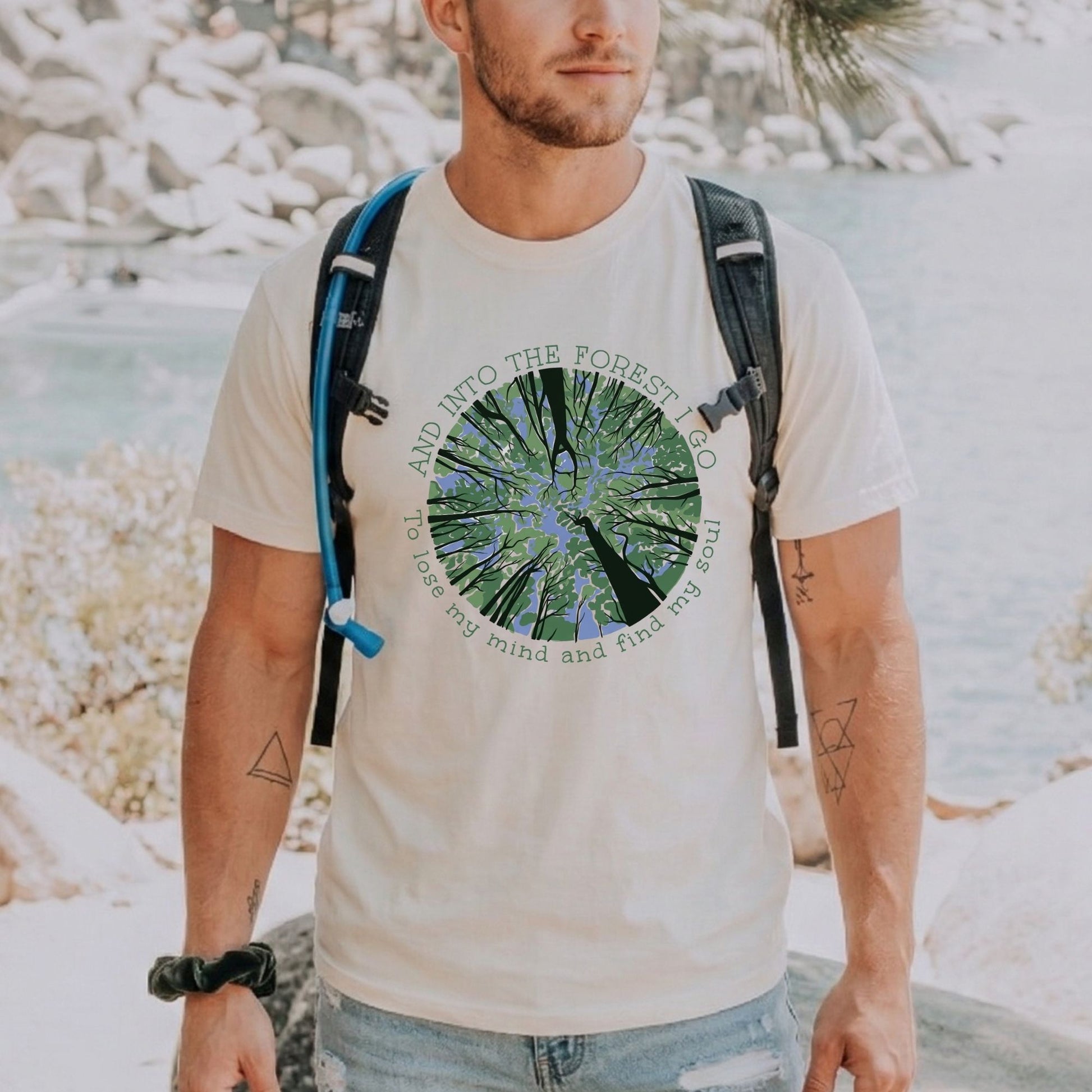 Man wearing a t-shirt with a nature forest graphic and text, standing near a river