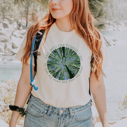 Woman wearing a white t-shirt with a nature forest graphic and text, standing in a forest.