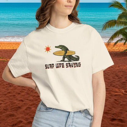 Person wearing a white t-shirt with a graphic design of a croc holding a surfboard and text 'Surf Life Saving'.