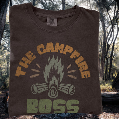 The CampFire Boss Black Tshirt Folded on a forest background