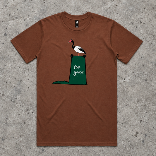A brown short-sleeve crewneck t-shirt featuring a graphic of a black and white goose with a red beak perched on top of a green trash can containing the text 'you goose'.