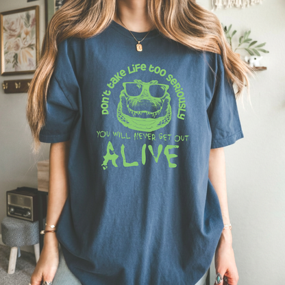 Crocodile T-shirt featuring a green sunglasses-wearing crocodile graphic with the quote “Don’t take life too seriously, you will never get out alive” on a blue tee.