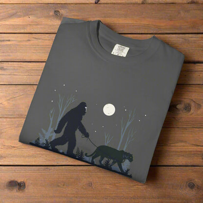 Folded gray t-shirt with a graphic of a bigfoot and a panther walking under a moonlit sky.