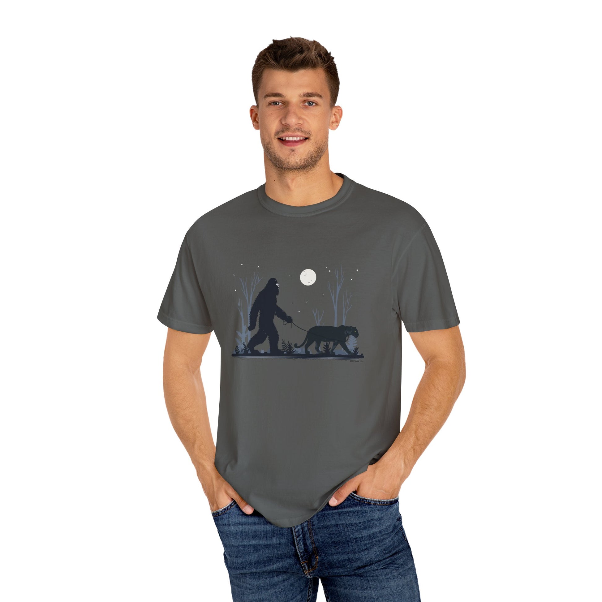 Man wearing a gray t-shirt with a graphic design of a Yowie Bigfoot and Panther walking under a moonlit sky.