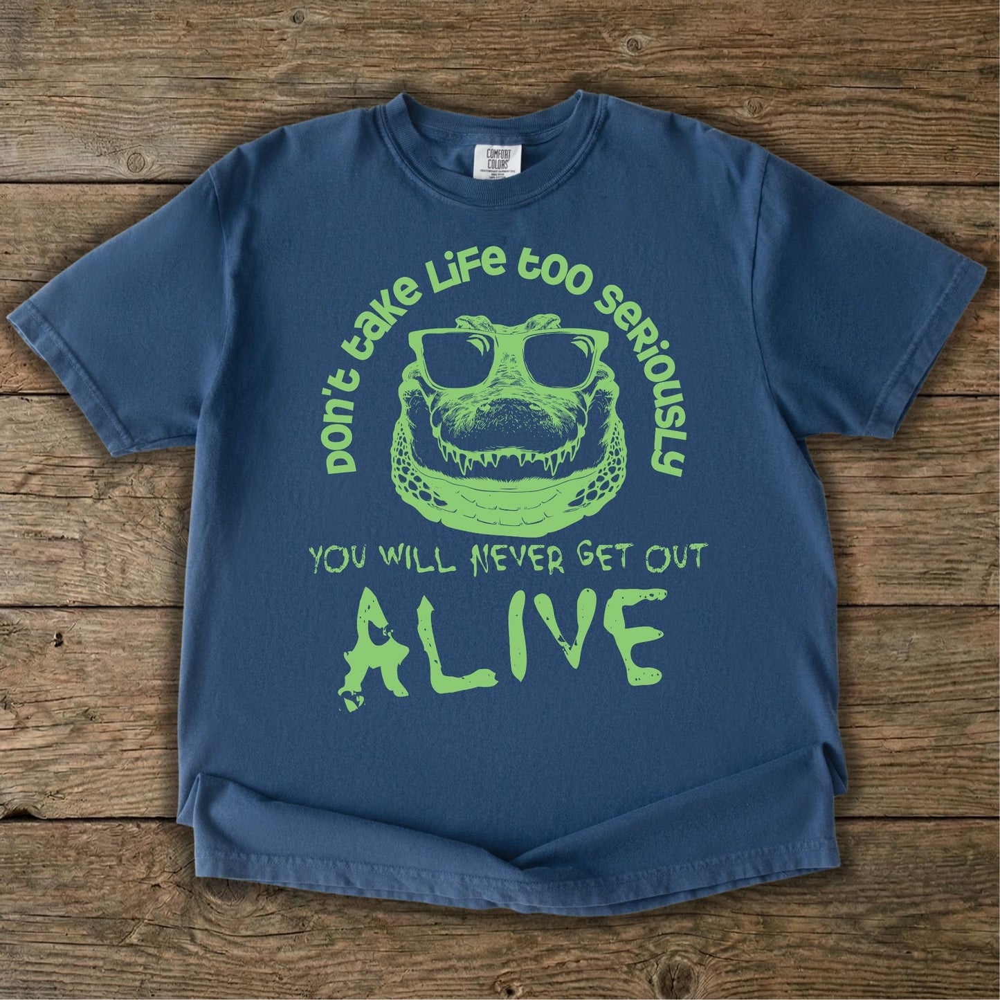 Crocodile T-shirt featuring a green sunglasses-wearing crocodile graphic with the quote “Don’t take life too seriously, you will never get out alive” on a blue tee.