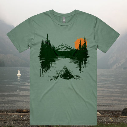 Green kayaking adventure T-shirt with canoe on mountain lake design, featuring pine trees, distant peaks, and orange sunset -GhostGum Tees