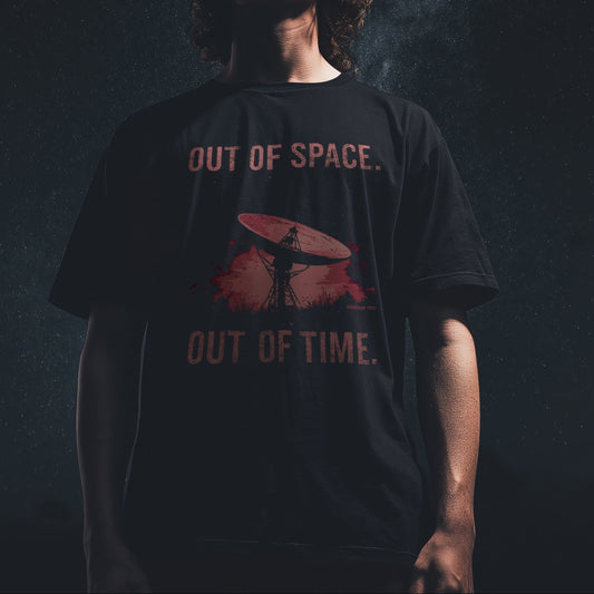 Model wearing a black T-shirt with “Out of Space. Out of Time.” design featuring a satellite dish under a cosmic night sky, moody lighting, space-inspired vibe