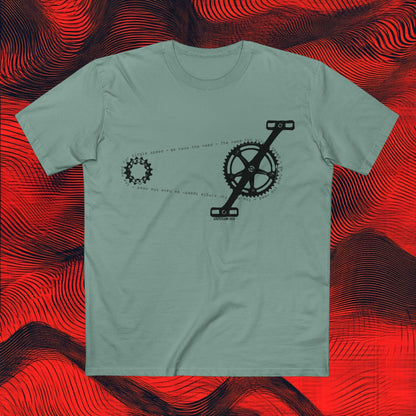 Sage green graphic t-shirt featuring a black bike crank and cog design with the text "The Need for Single Speed" in a circular path, displayed on a red abstract background.
