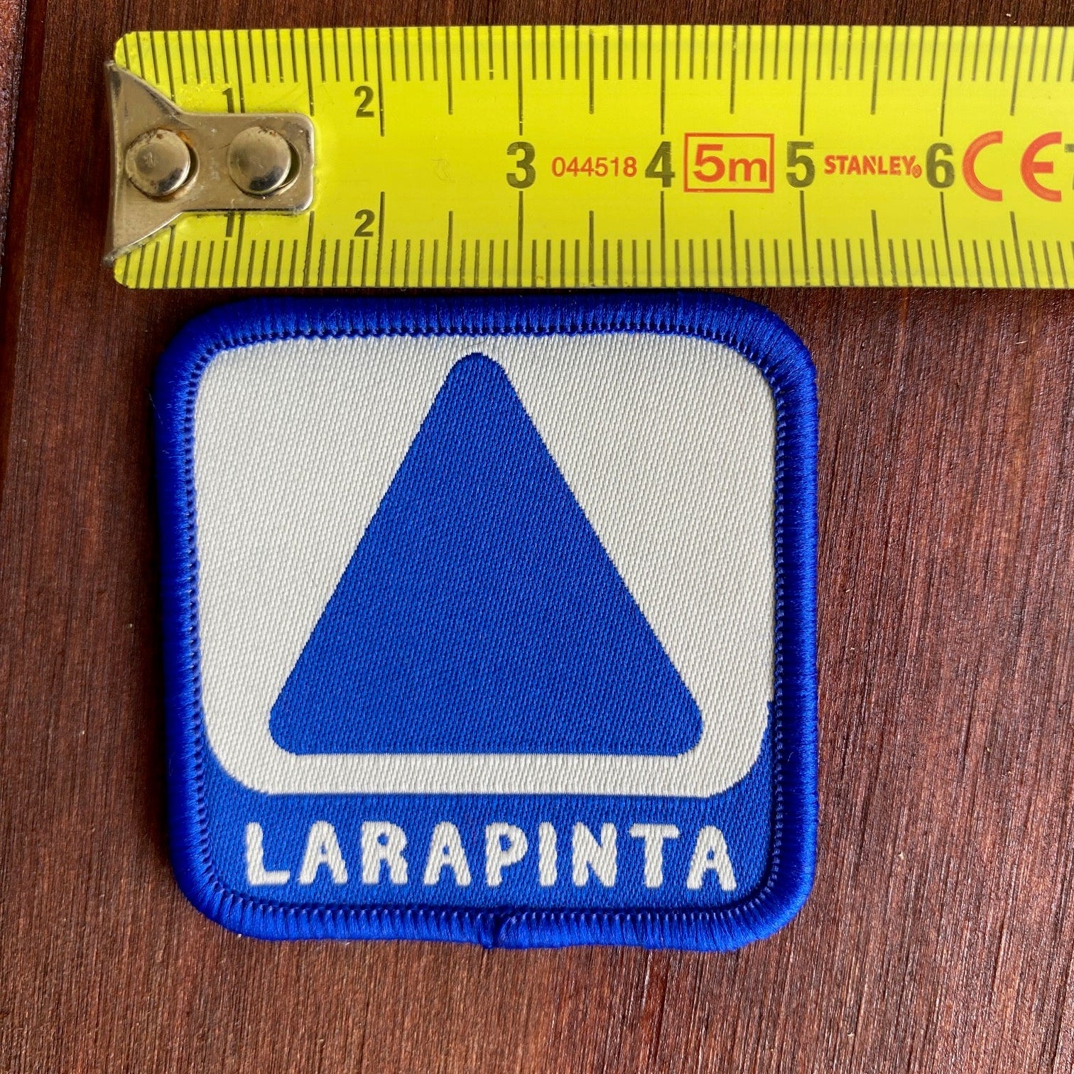 Patch with blue and white design and 'LARAPINTA' text, measured against a ruler on a wooden surface.