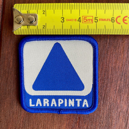 Patch with blue and white design and 'LARAPINTA' text, measured against a ruler on a wooden surface.