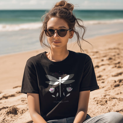 Woman on a beach wearing sunglasses and a black graphic t-shirt featuring a dragonfly and flowers with the text “Dry Season Vibes” – stylish summer women’s adventure tee.